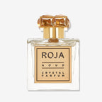 Aoud CRYSTAL™️ by Roja Parfums is a clear glass perfume bottle with a gold cap adorned by two gem-like decorations and a gold-bordered label, capturing luxury with opulent Saffron & Rose Oud notes.